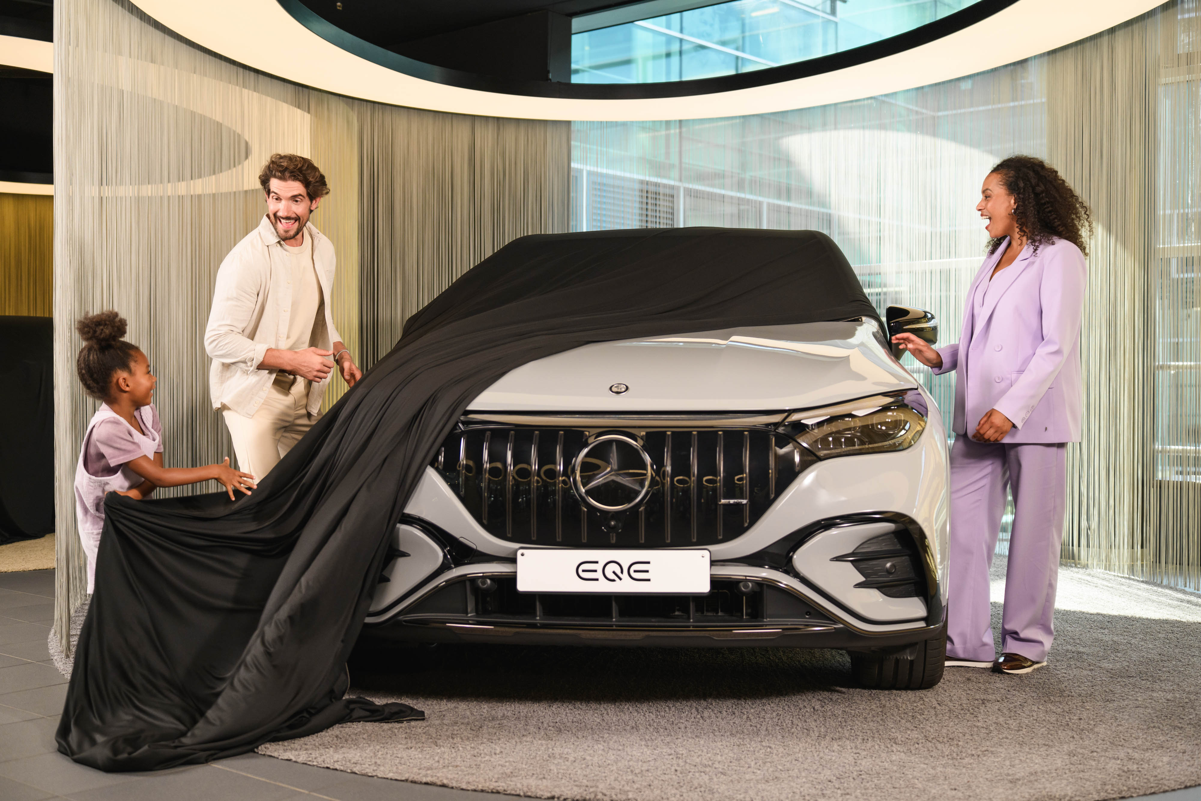 Finance offer for your Mercedes-Benz Two people and a child removing a cover off a new Mercedes-Benz vehicle in a showroom.