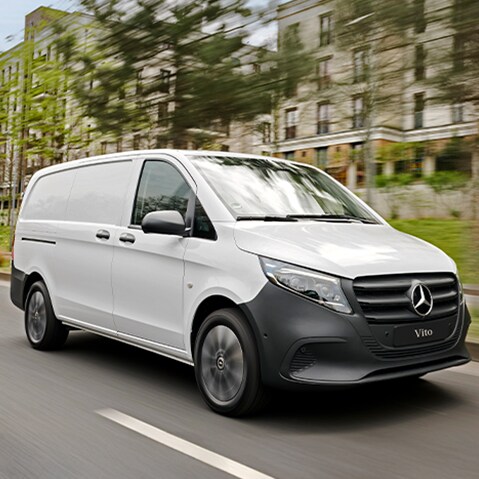 The Mercedes-Benz Sprinter Panel Van is driving on the street in front of a building.   