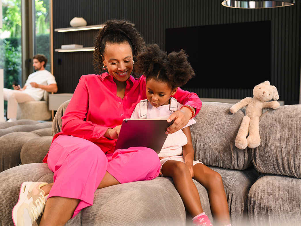 Finance overview | Customer portal A person and child sitting on a sofa using a mobile device, with another person sitting in the distance.