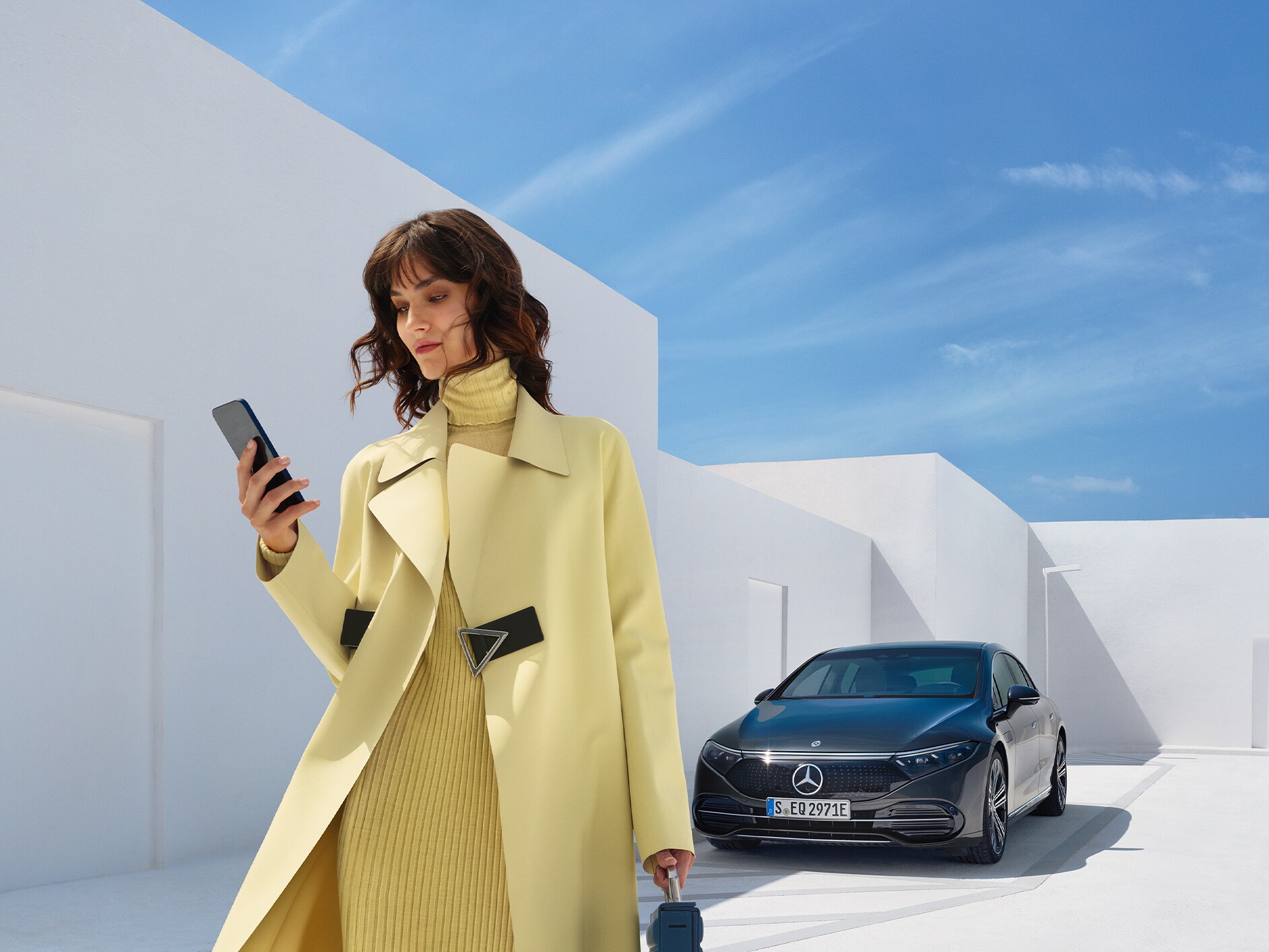 Woman looking at her cell phone as she walks away from her Mercedes-Benz with EQ technology.