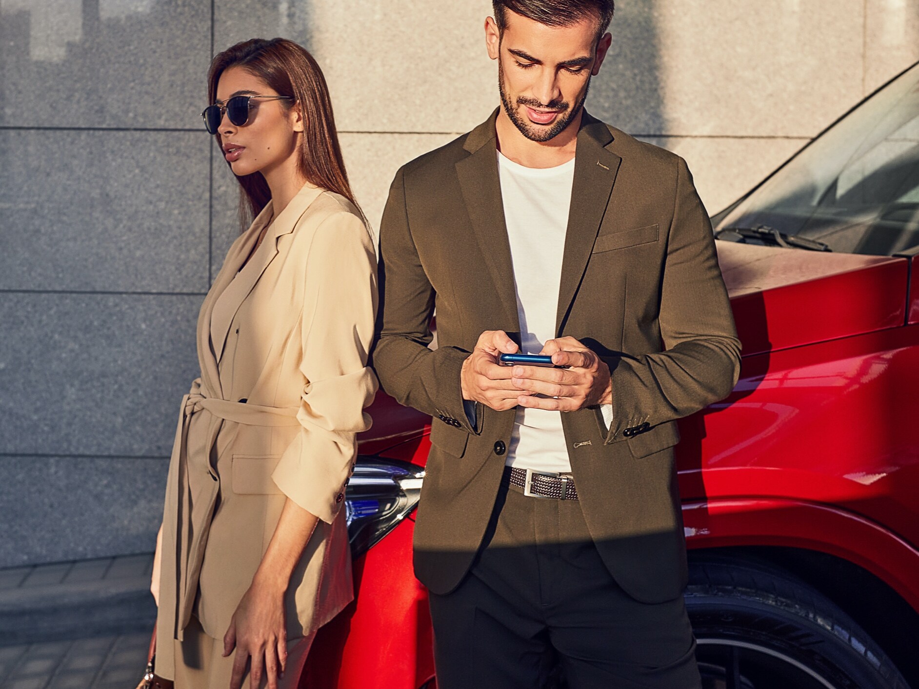 A woman and a man are leaning against a Mercedes-Benz. The man is connected to the vehicle via smartphone and Digital Extras.