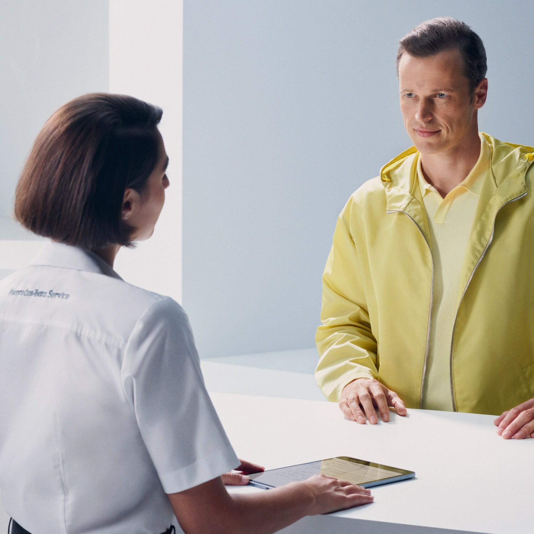 A customer leaning at the counter turns expectantly to face a Mercedes-Benz employee.