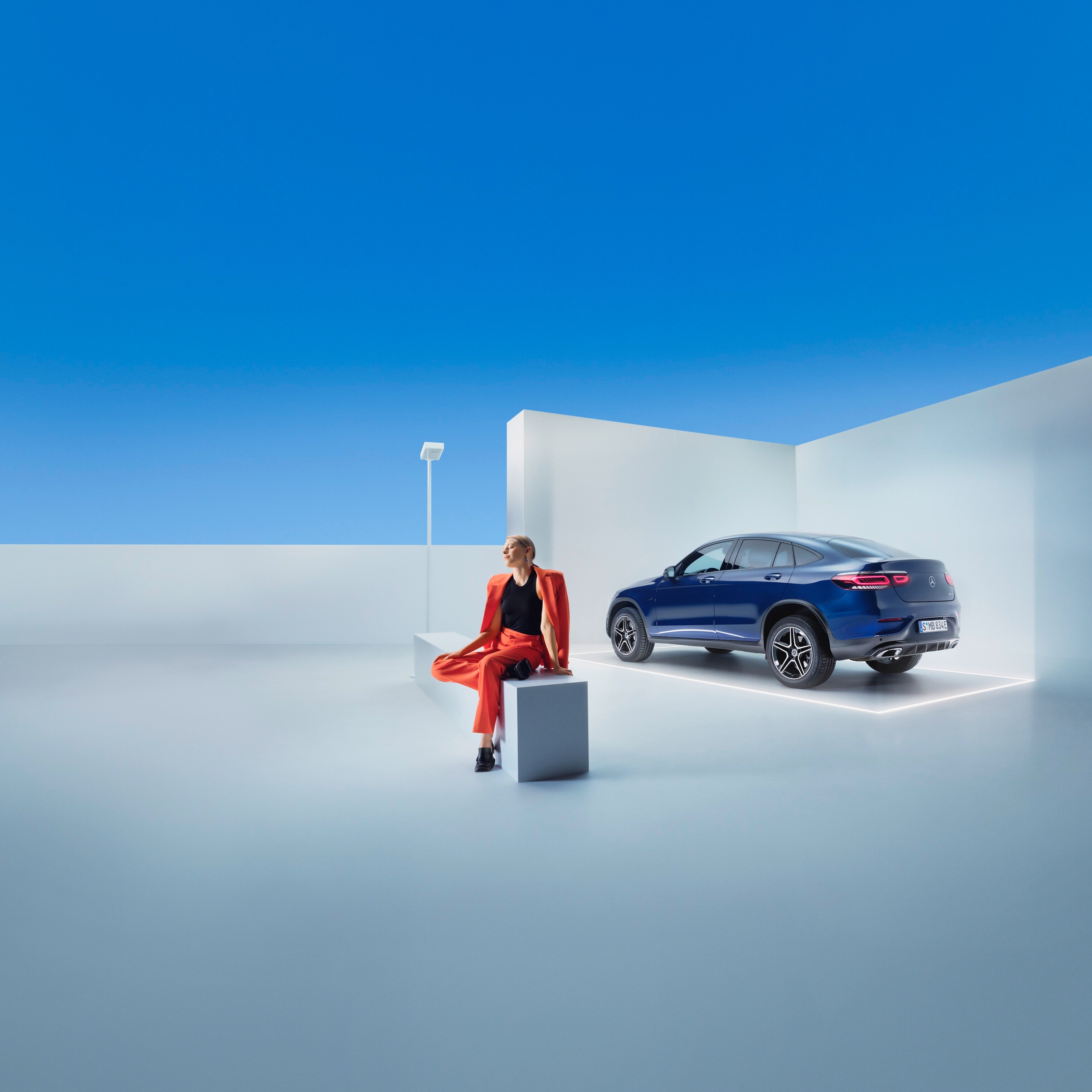 A woman sits on a bench in front of a Mercedes-Benz.