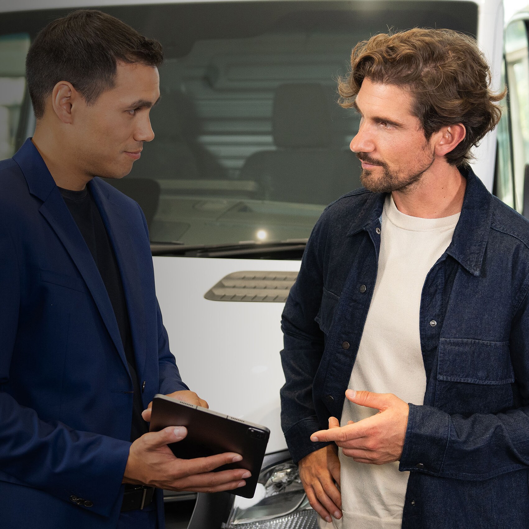 Two people talking and pointing at a mobile device while standing in front of a Mercedes-Benz van.