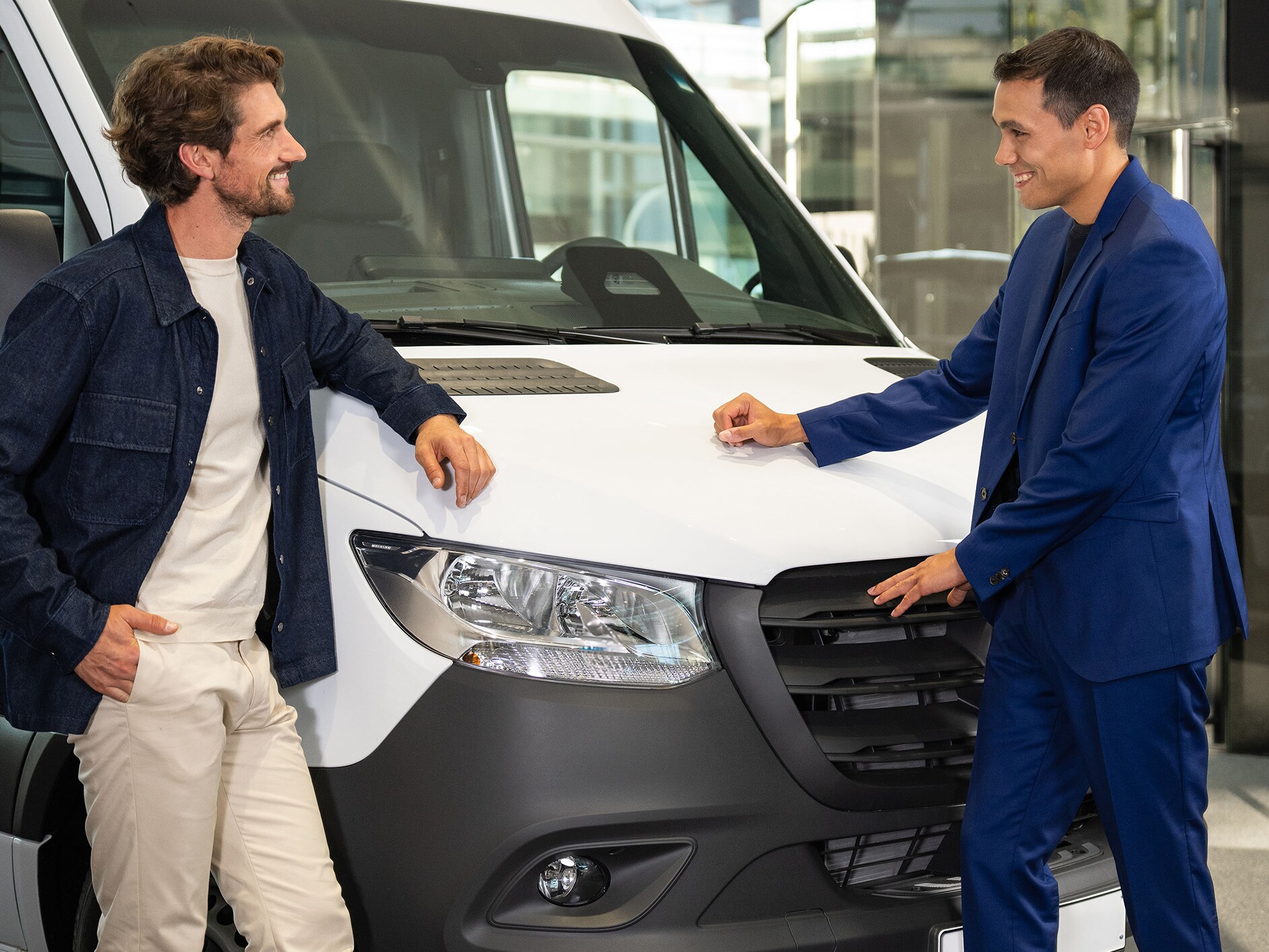 Two people leaning against a Mercedes-Benz van and having a conversation.
