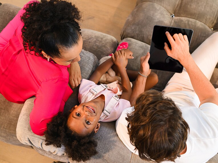 High angle shot of two people looking at a mobile device with a child between them, looking into the camera